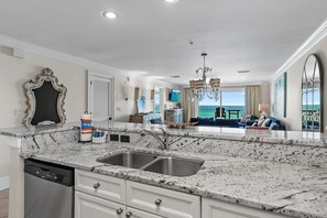 A kitchen with a granite countertop, stainless steel sink, and a dishwasher. - Crystal Dunes 304 (Destin)