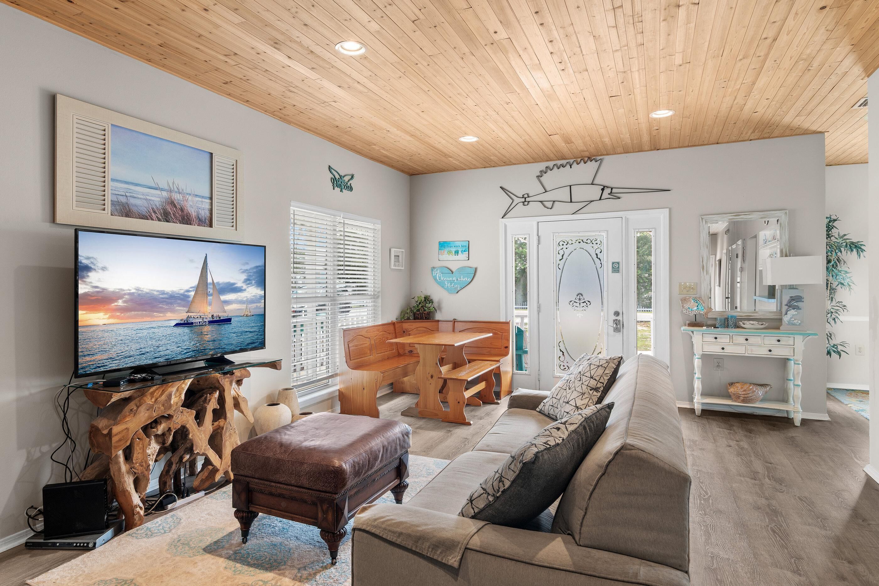 A living room with a wooden ceiling, a television displaying a sailboat, a wooden bench, a sofa, and a console table with decorative items.