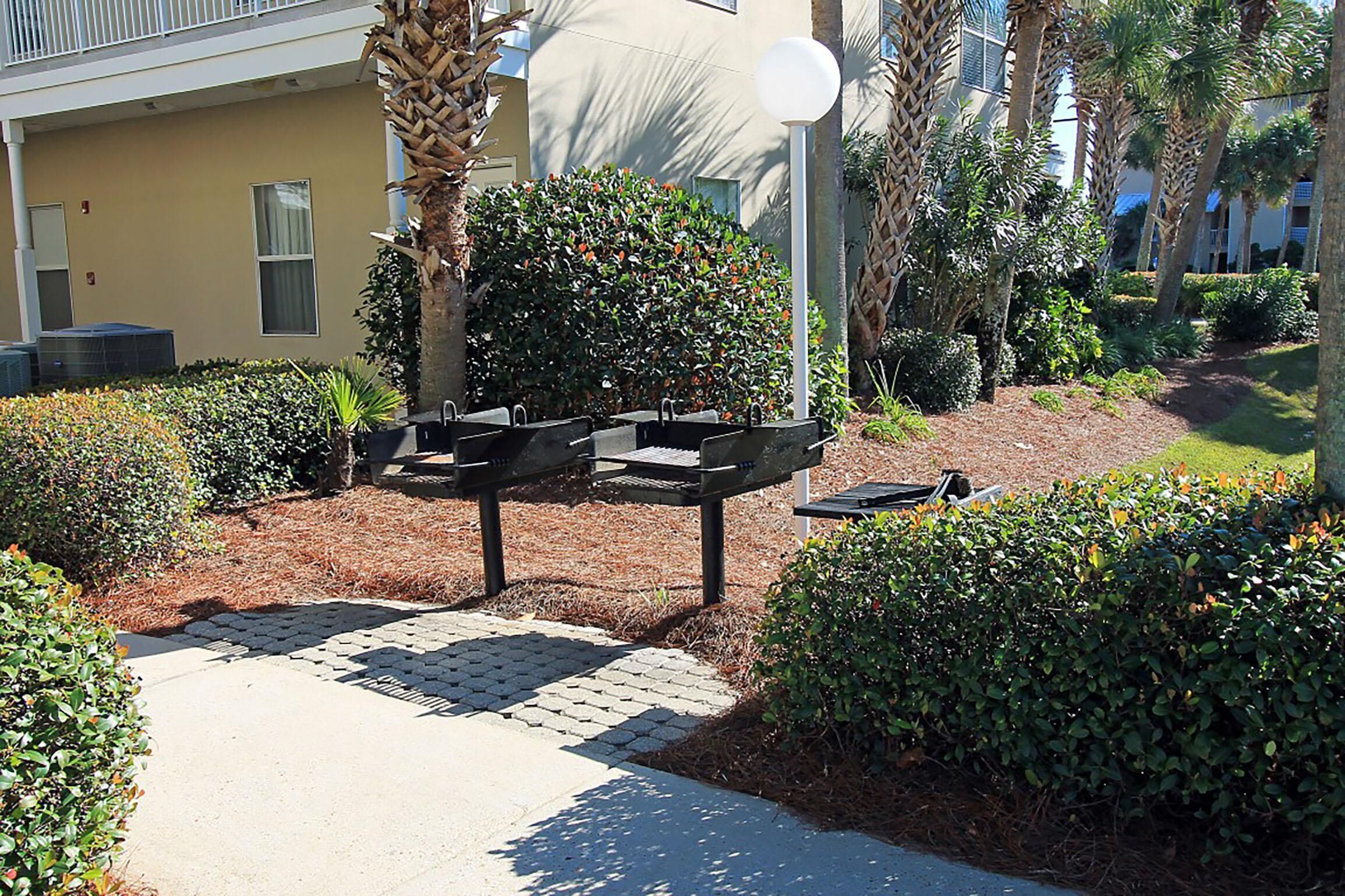 An outdoor seating area with tables and chairs, surrounded by well-maintained hedges and palm trees.