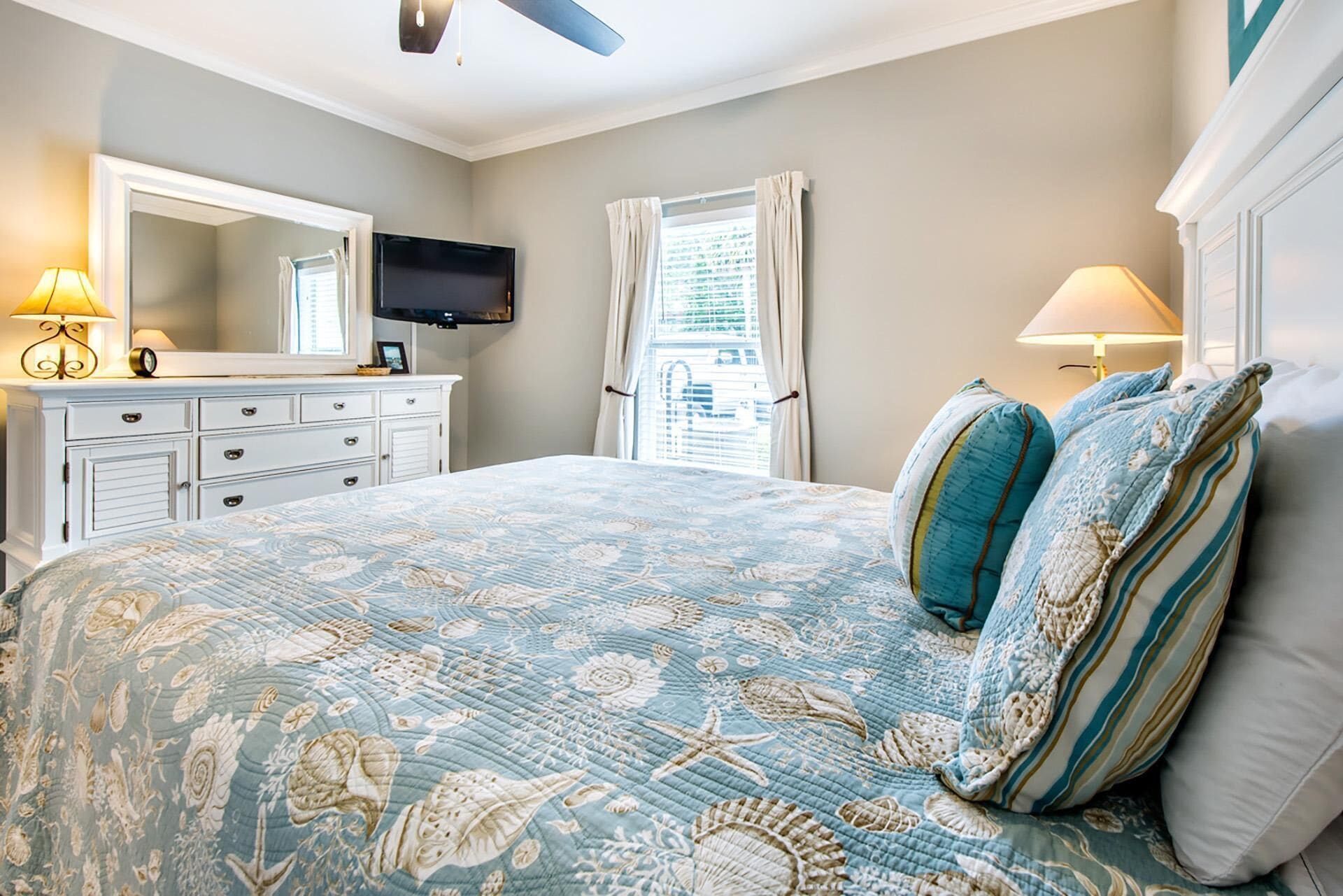 A bedroom with a bed, a dresser, a TV, and a window with curtains.