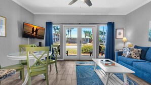 A living room with a television, a blue sofa, a dining table with chairs, and a ceiling fan. - Caribbean Dunes 120 (Destin)