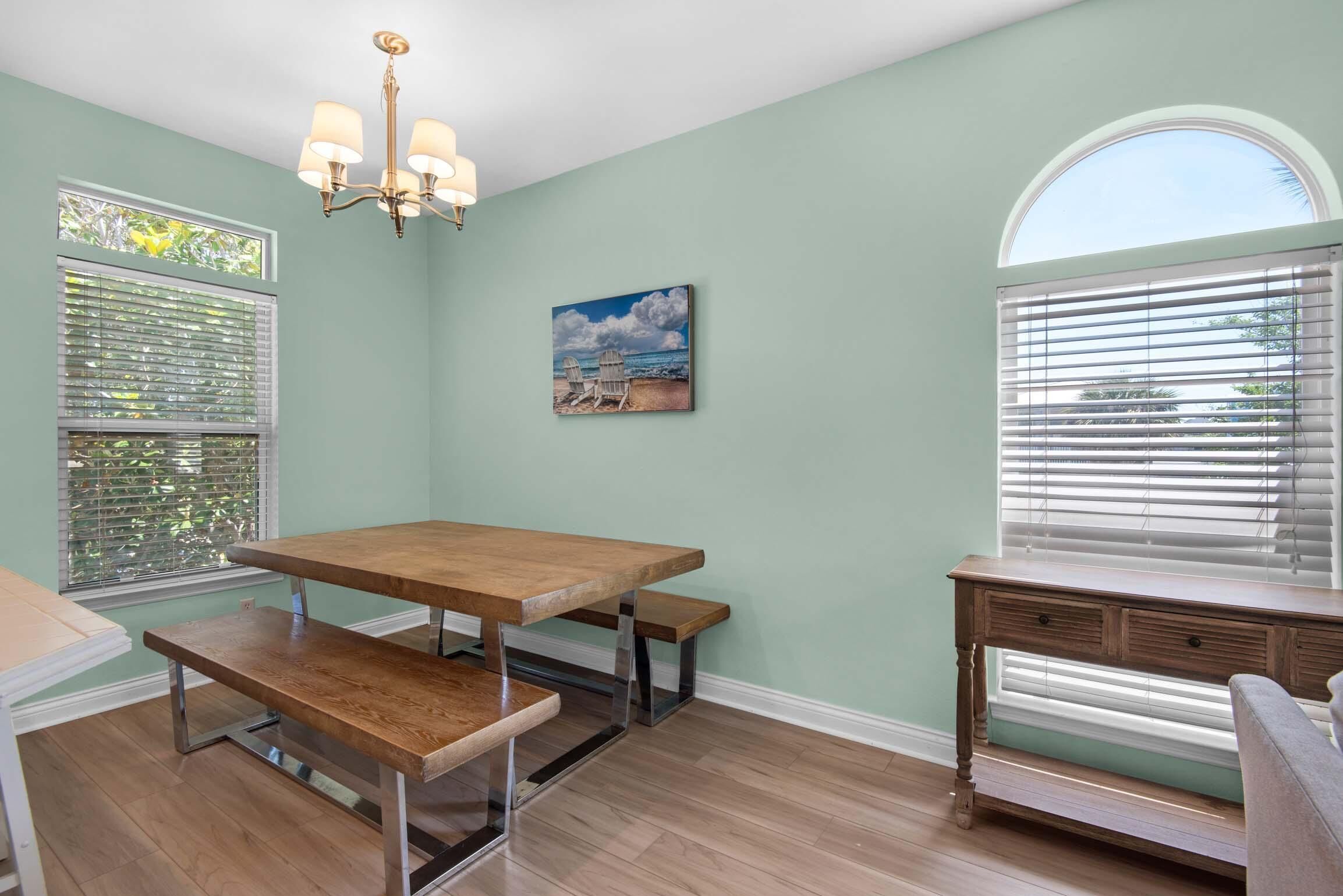 A dining area with a wooden table and benches, a chandelier, and a painting of beach chairs.