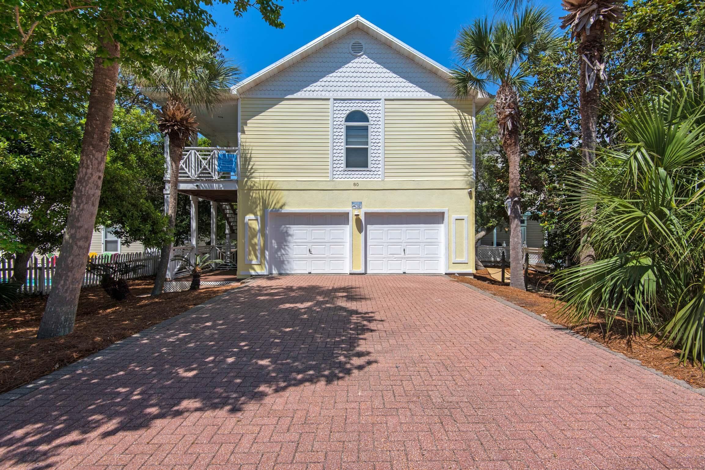 A two-story building with a garage, surrounded by trees and a paved driveway.