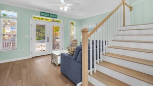Een woonkamer met een trap, een plafondventilator en een deur met de tekst 'Beach House'.