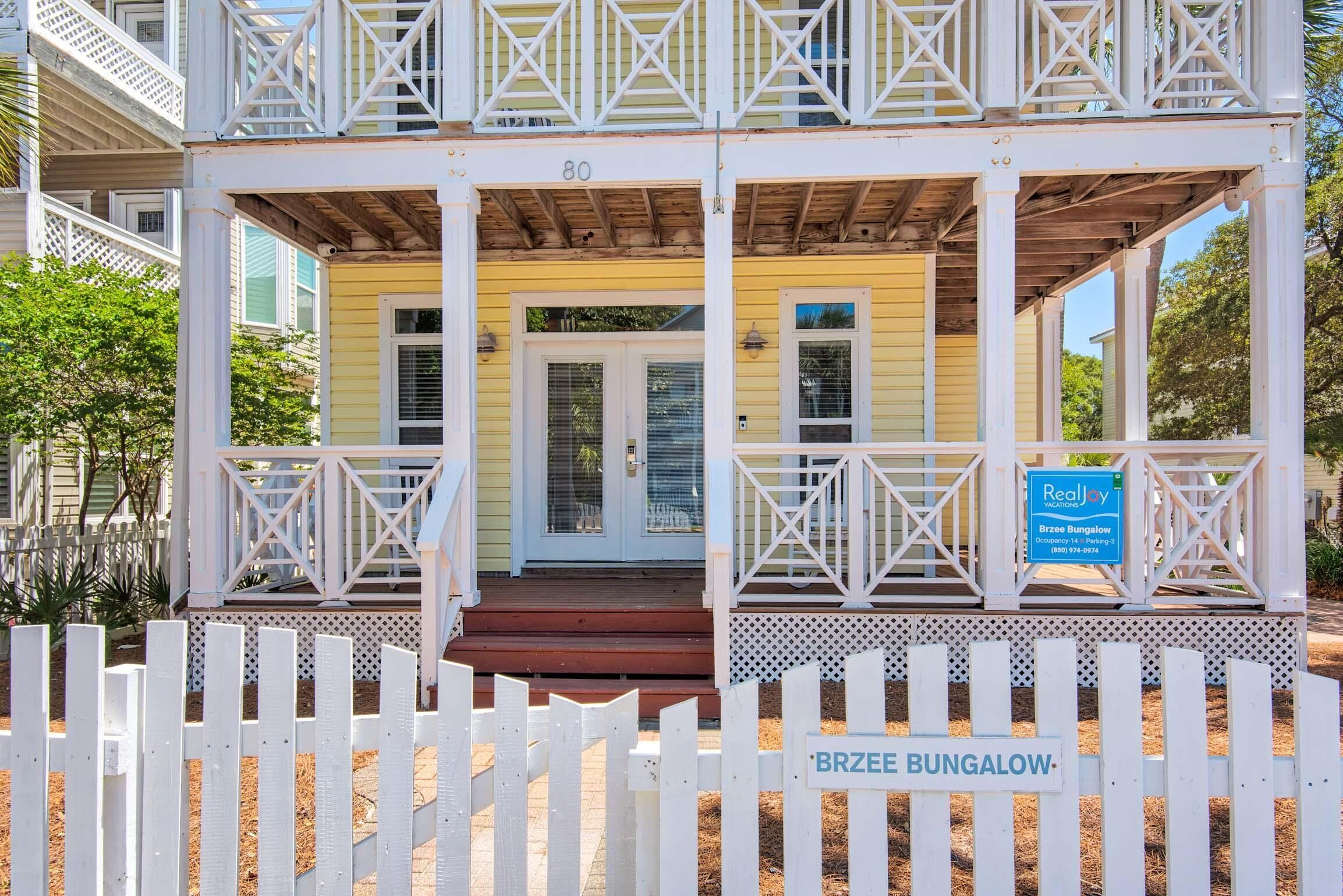 A two-story building with a porch, a sign for Brzee Bungalow, and a white picket fence.
