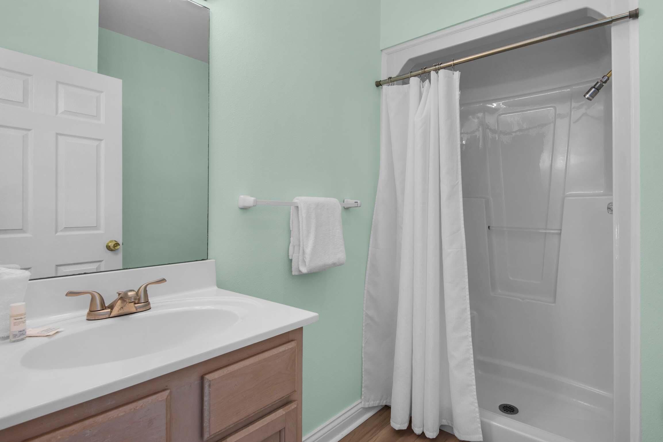 A bathroom with a white sink, a mirror, a shower with a white curtain, and a towel rack.