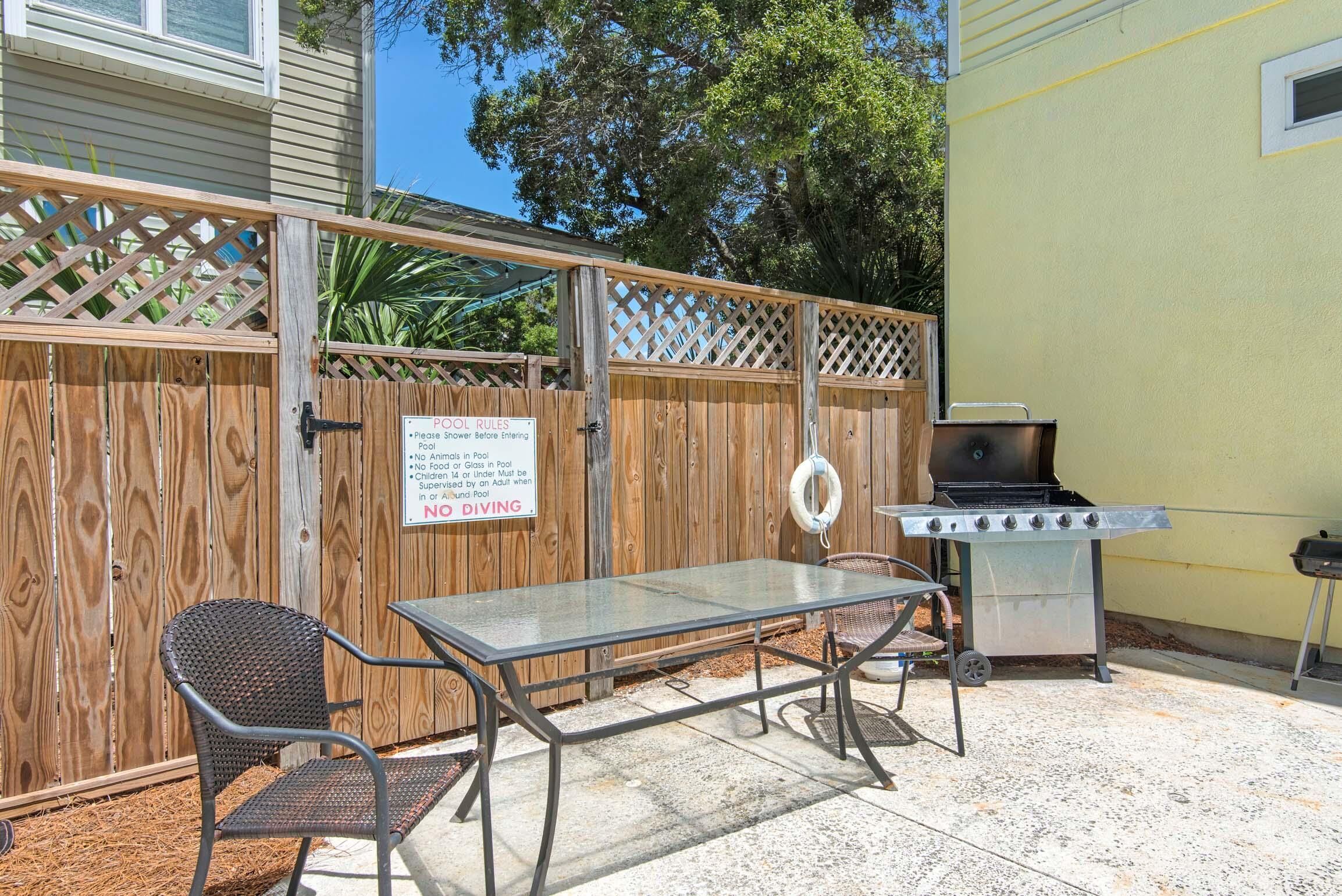An outdoor patio with a metal table and chairs, a grill, and a wooden fence with a sign.