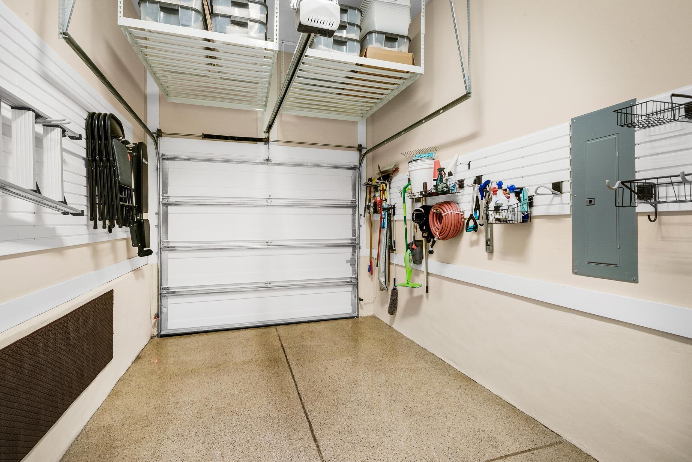 Un garage propre et bien rangé, avec une porte de garage fermée, des étagères contenant des produits de nettoyage et une boîte à outils fixée au mur.