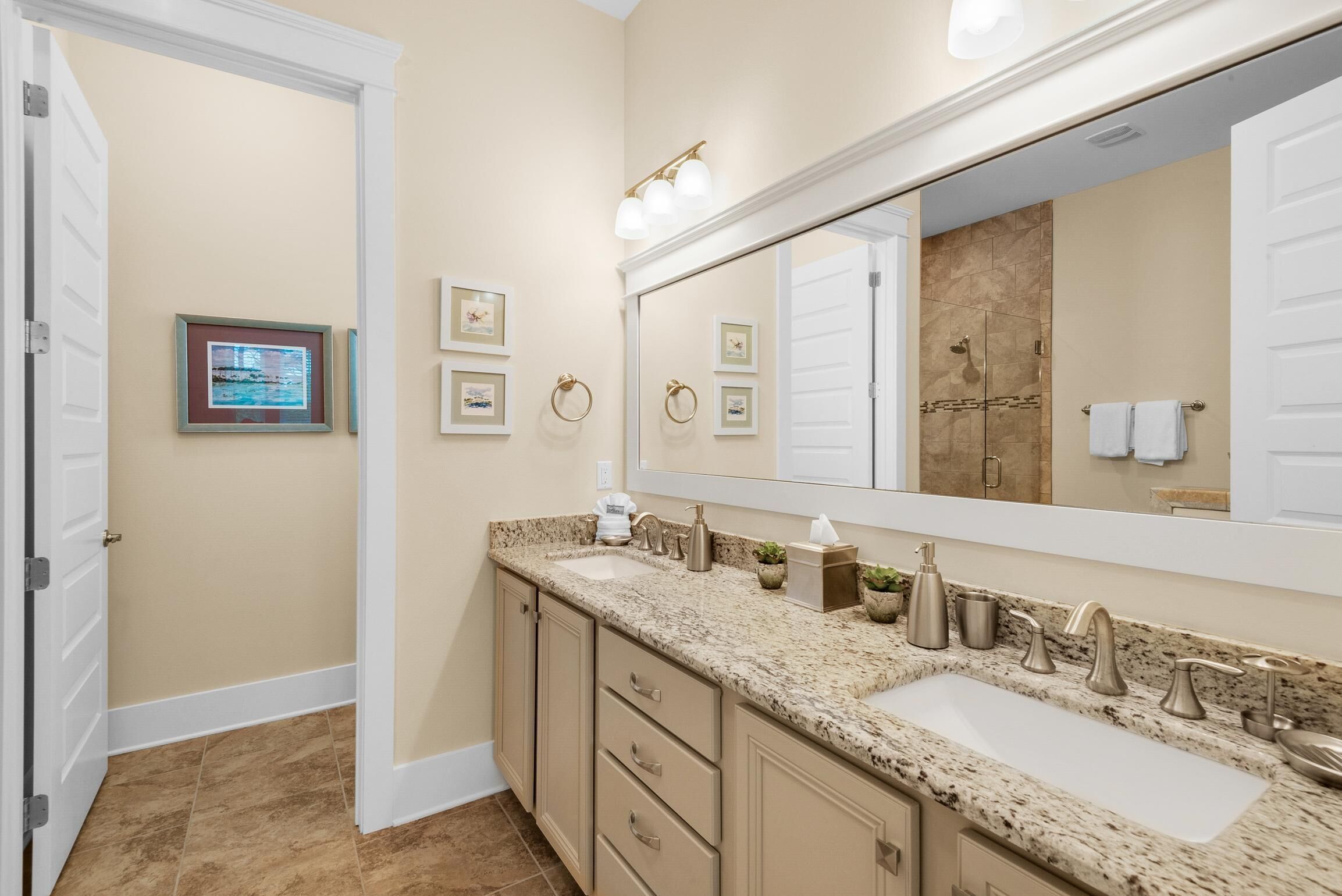 A bathroom with a double sink vanity, a large mirror, and framed pictures on the wall.