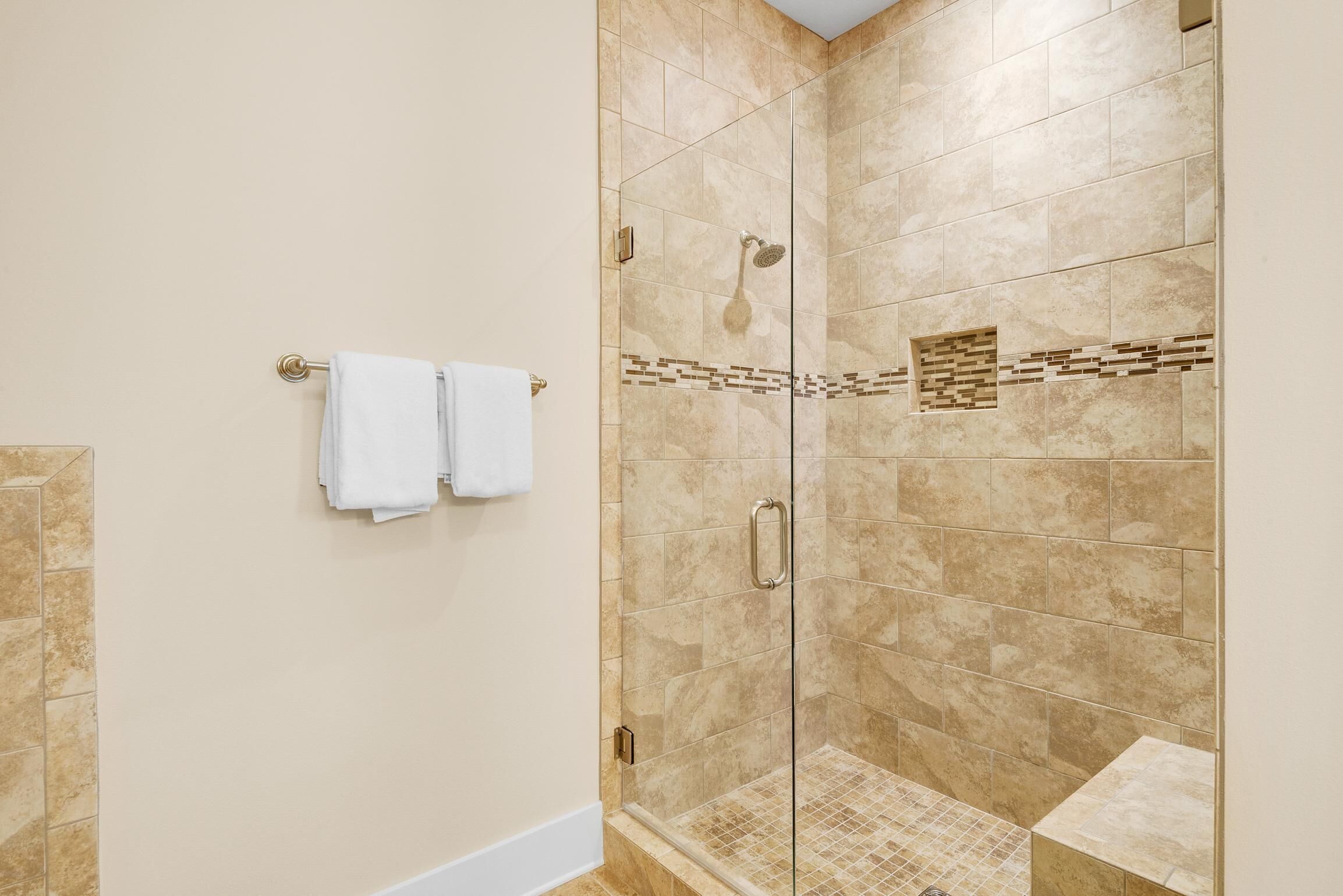 Une douche fermée par des parois de verre, avec des carreaux de couleur beige et un petit motif décoratif sur le mur.