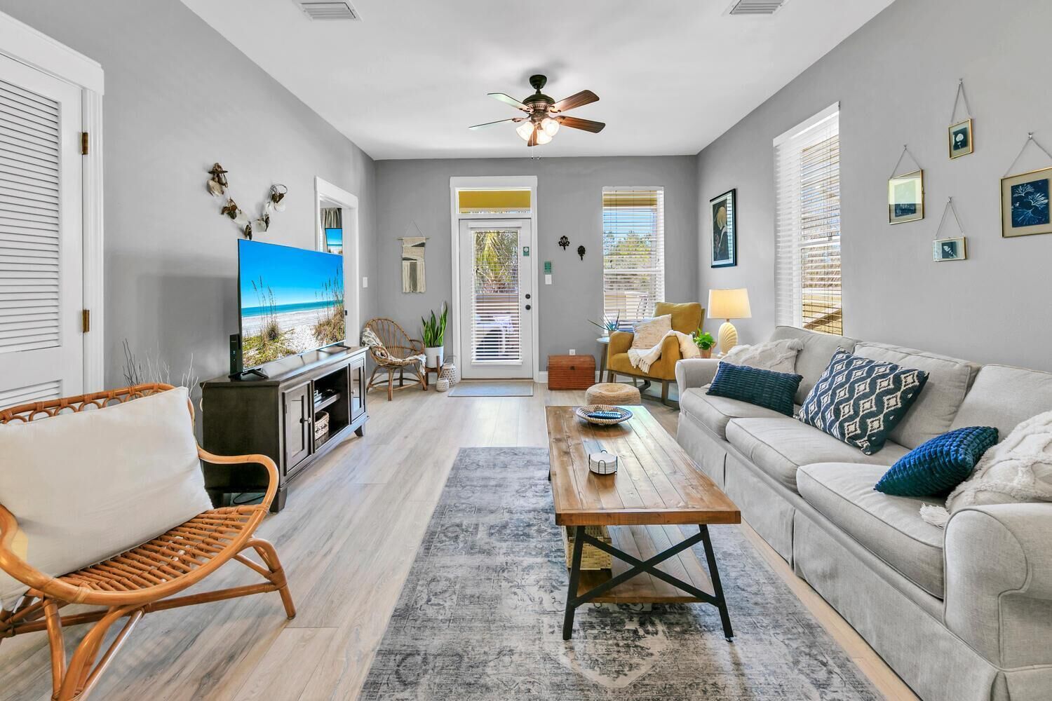 A living room with a sofa, coffee table, and TV, a ceiling fan, and a view of the outdoors through a door.