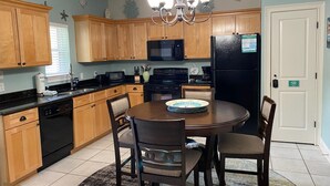 A kitchen with wooden cabinets, a black refrigerator, a microwave, and a dining table with chairs. - Topsail Village 211- Sandy Feet Retreat (Santa Rosa Beach)