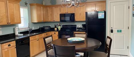 A kitchen with wooden cabinets, a black refrigerator, a microwave, and a dining table with chairs.