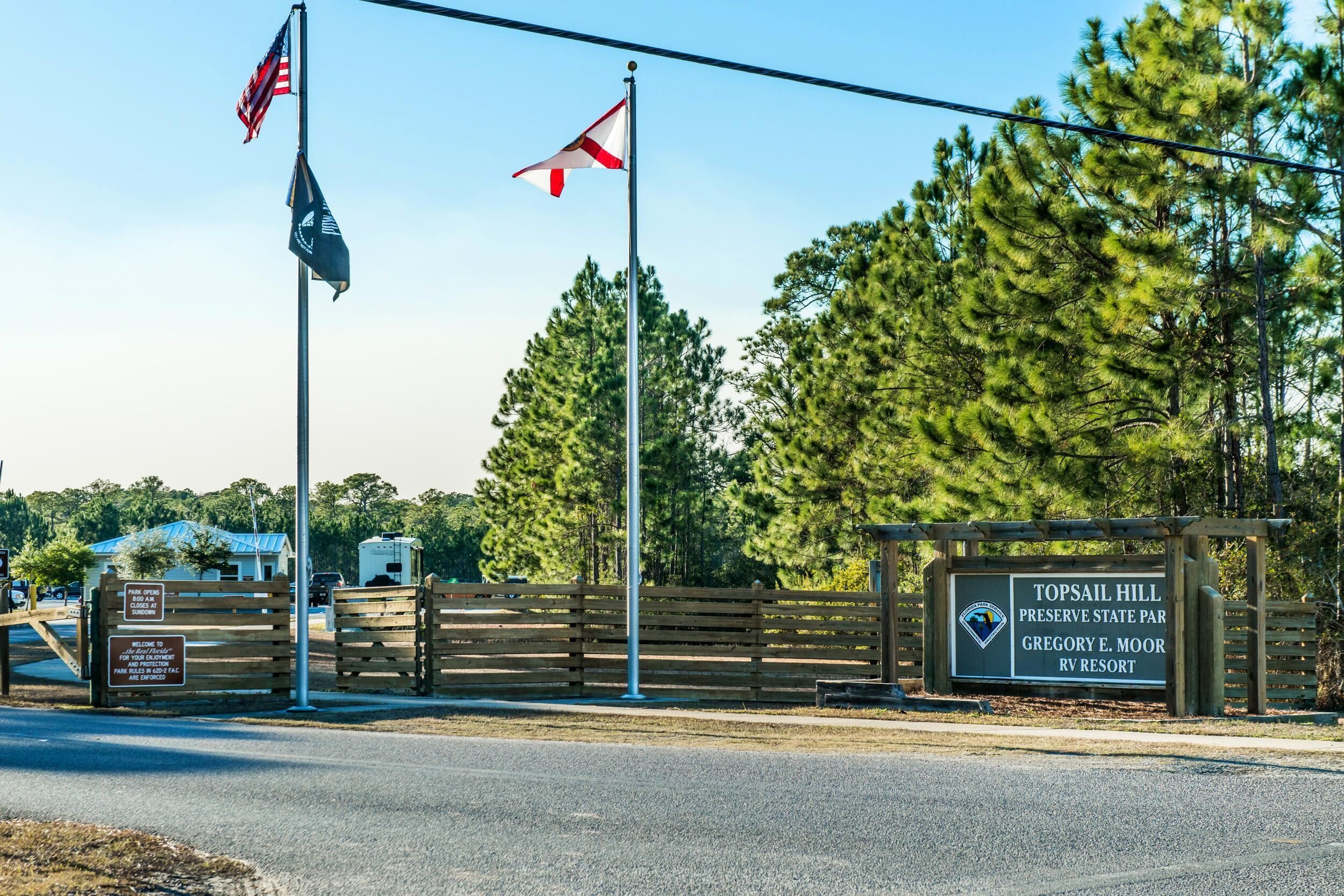 A sign for Topsail Hill Preserve State Park with a wooden fence and flags.