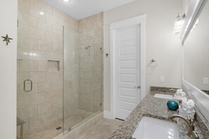 A bathroom with a glass-enclosed shower, a white door, a granite countertop, and a sink with a faucet. - The Light House (Santa Rosa Beach)
