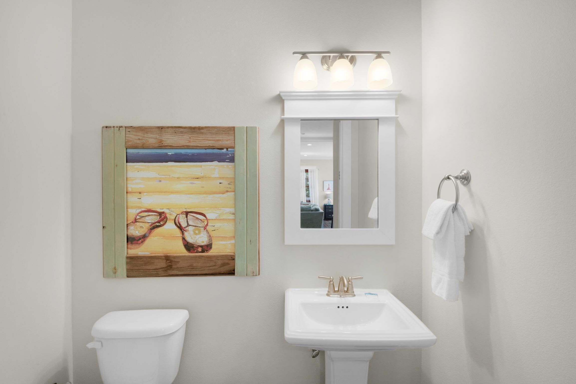 Ein Badezimmer mit Toilette und Waschbecken in Weiß, sowie einem Bild von Strandschuhen an der Wand.
