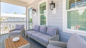 A covered porch with a wicker sofa, two chairs, and a wooden table. - The Graytest 30A Beach House (Santa Rosa Beach)