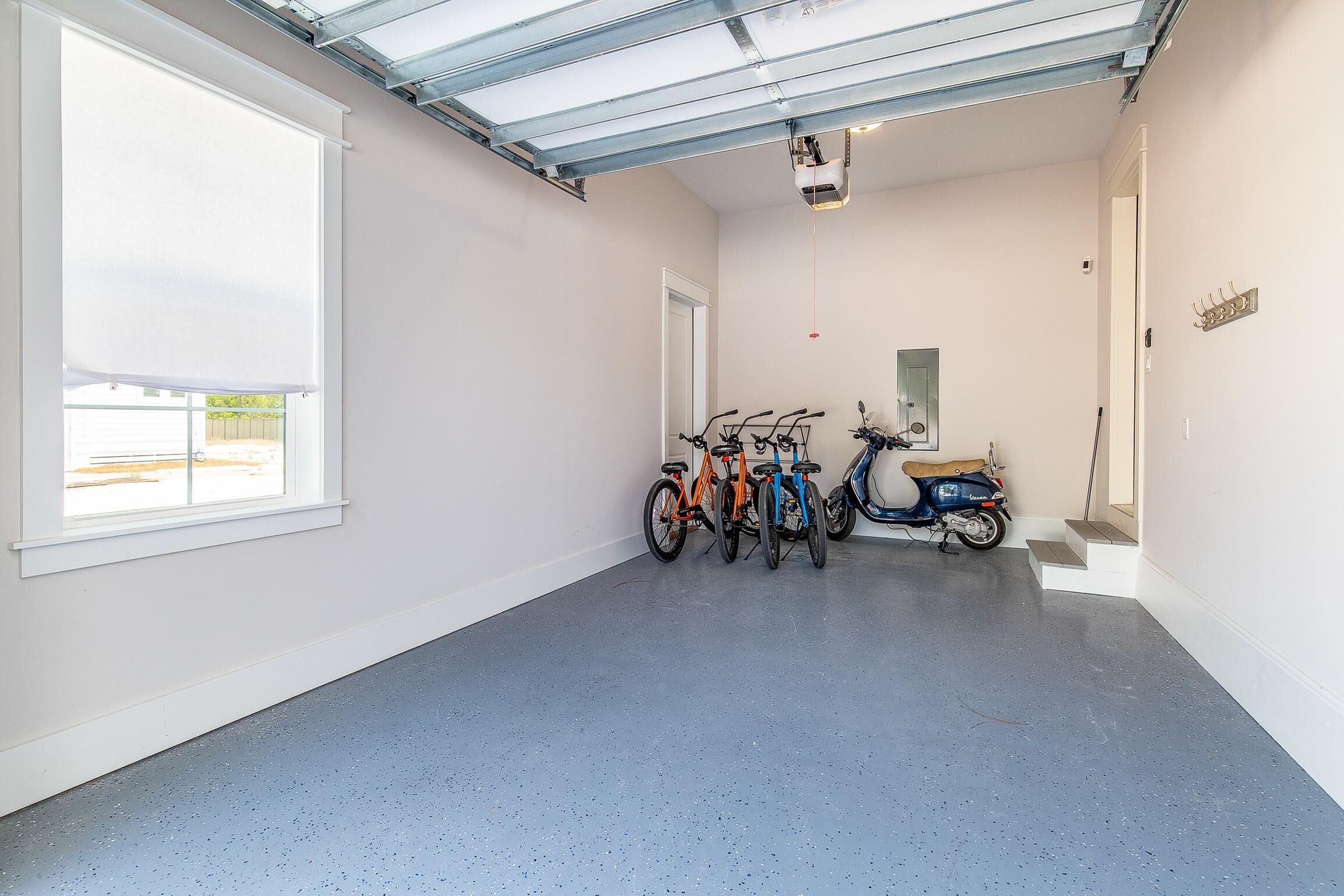 Un couloir propre et bien éclairé, avec un sol bleu à motifs, une grande fenêtre, ainsi que des vélos et un scooter garés contre le mur.