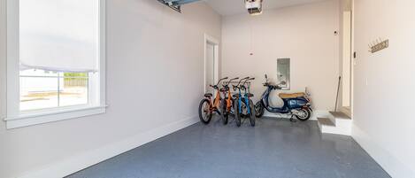 Un couloir propre et bien éclairé, avec un sol bleu à motifs, une grande fenêtre, ainsi que des vélos et un scooter garés contre le mur.