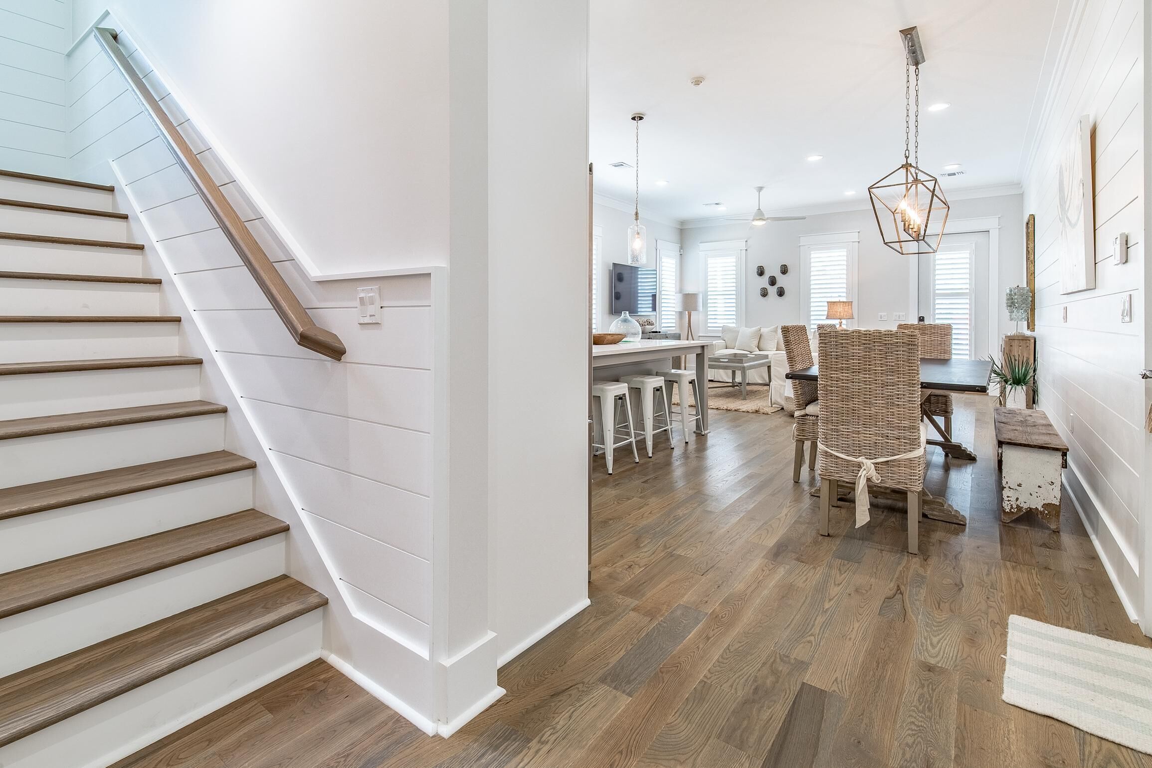 A staircase with wooden steps and white walls, leading to a dining area with wicker chairs and a wooden table.