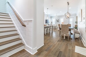 En trappe med trætrin og hvide vægge, der fører op til et spiseområde med fletstole og et træbord.