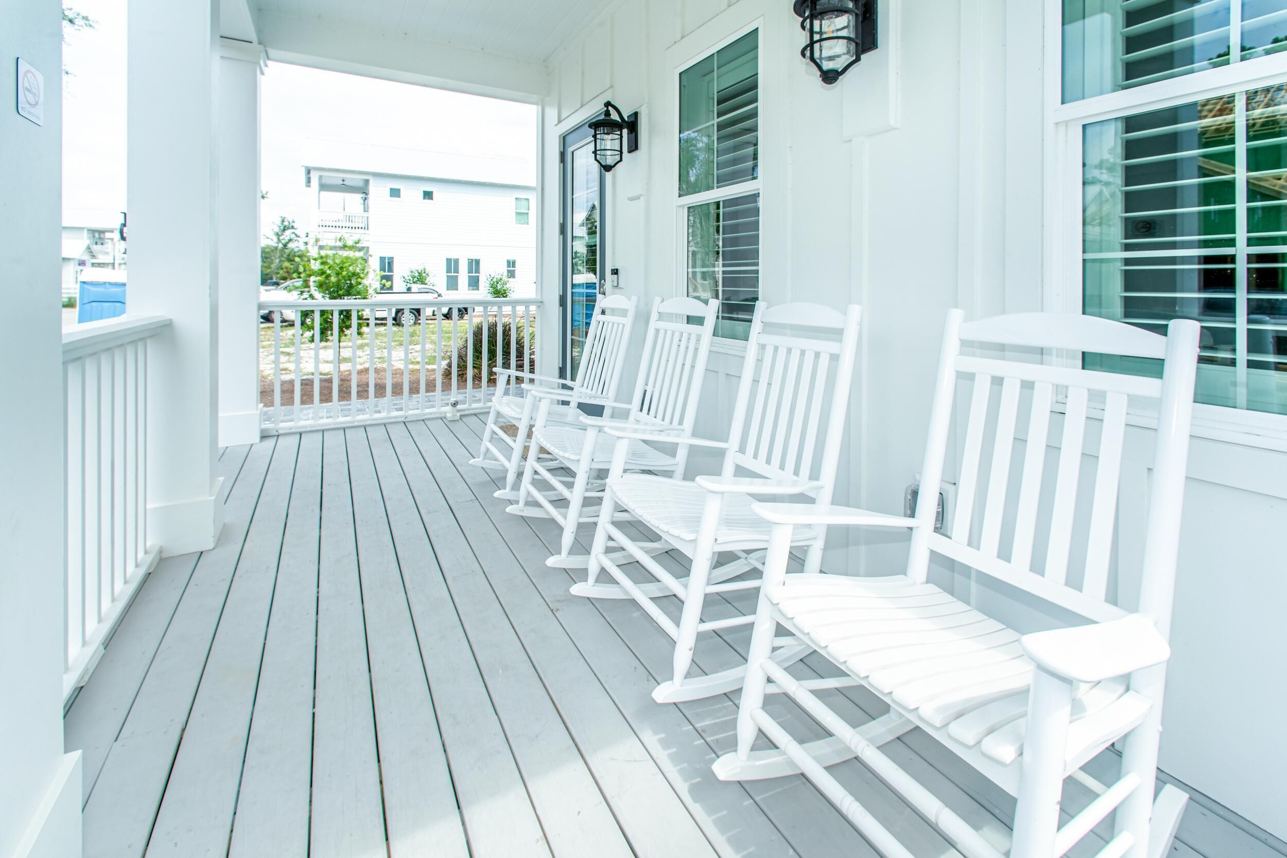 A porch with white rocking chairs and a white railing.