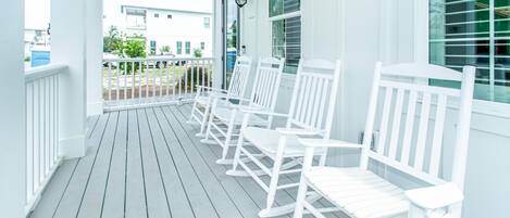A porch with white rocking chairs and a white railing.