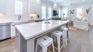 A modern kitchen with white cabinetry, a large island with stools, and pendant lighting. - The Graytest 30A Beach House (Santa Rosa Beach)