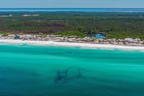 An aerial view of a coastal area with a beach, clear turquoise waters, and dense forested land. - Surfin' Turtle (Santa Rosa Beach)