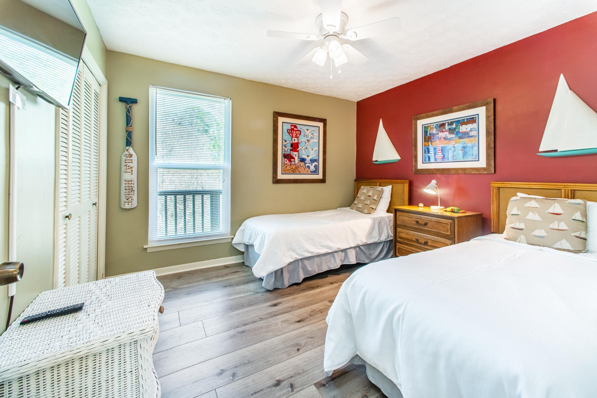A bedroom with two beds, a wooden floor, a ceiling fan, and a window with blinds.
