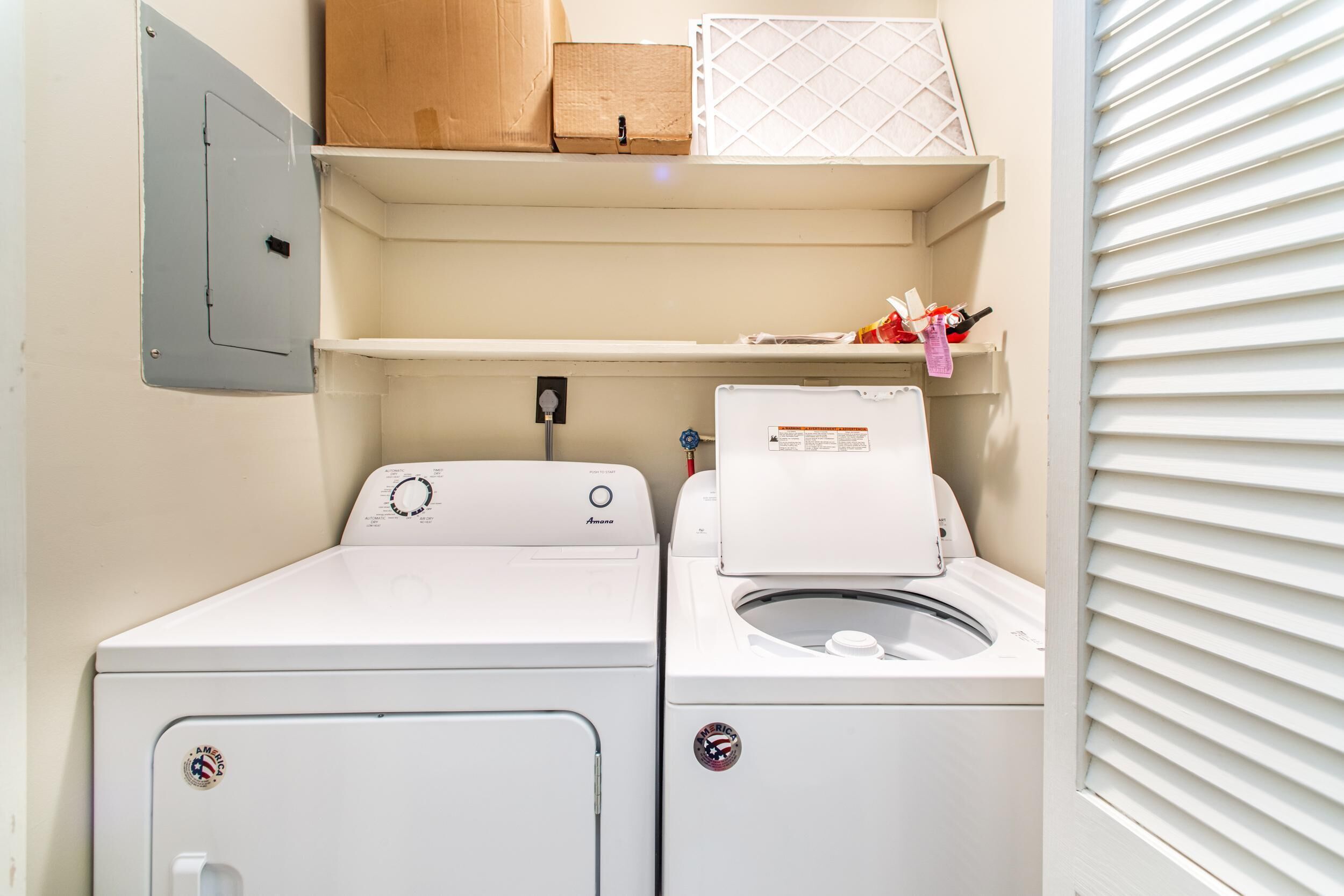 A laundry area with two white washing machines, a shelf with boxes, and a power outlet.