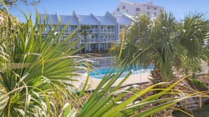 Ein Hotel mit Pool, umgeben von Palmen und blauem Himmel.