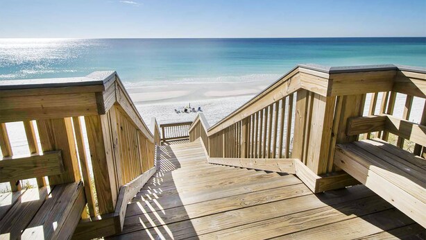 Eine Holzterrasse führt zu einem Strand mit freiem Blick auf das Meer.
