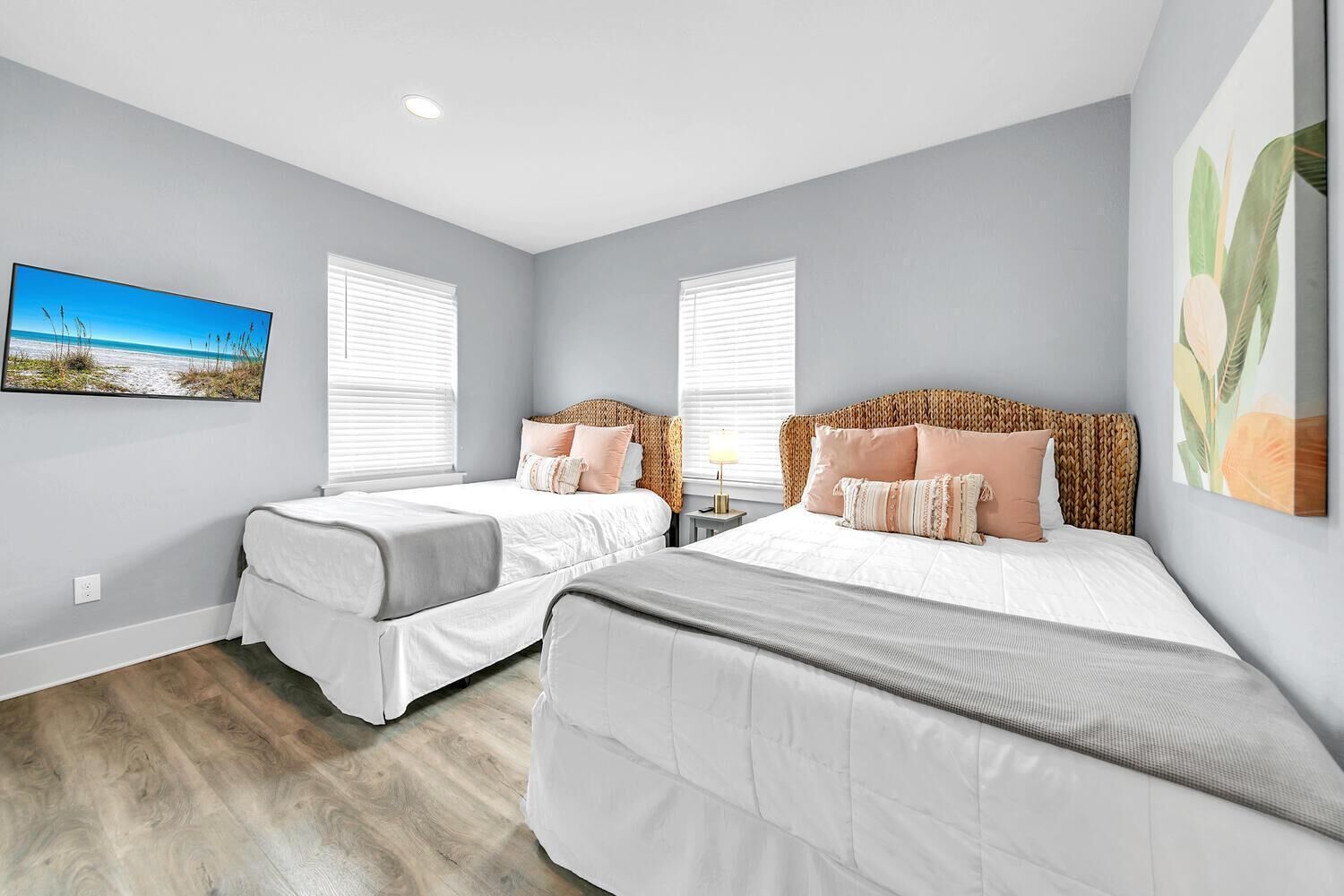 A bedroom with two beds, a large window, and a painting on the wall.