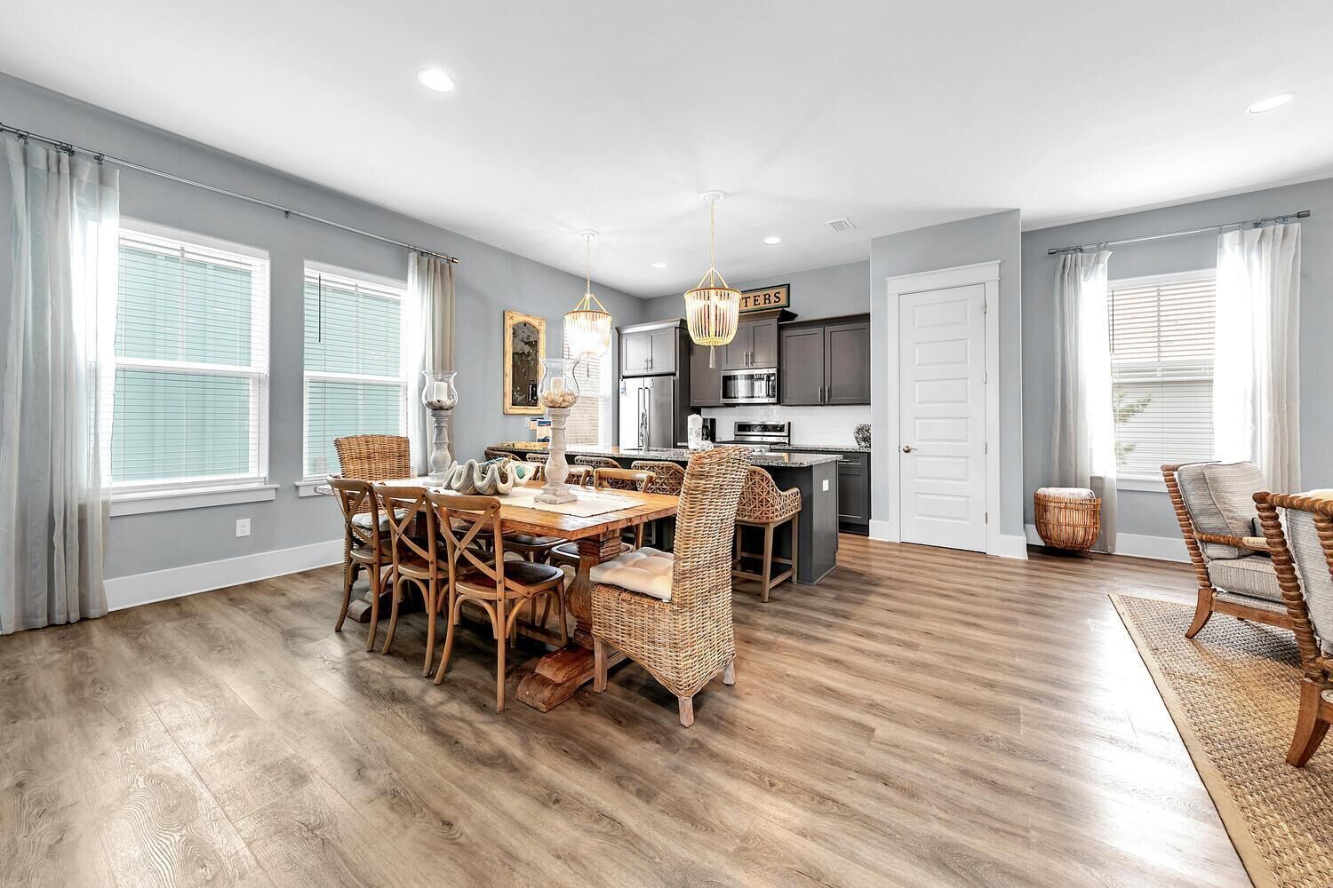 A spacious dining area with a wooden table and wicker chairs, a kitchen with modern appliances, and large windows with curtains.