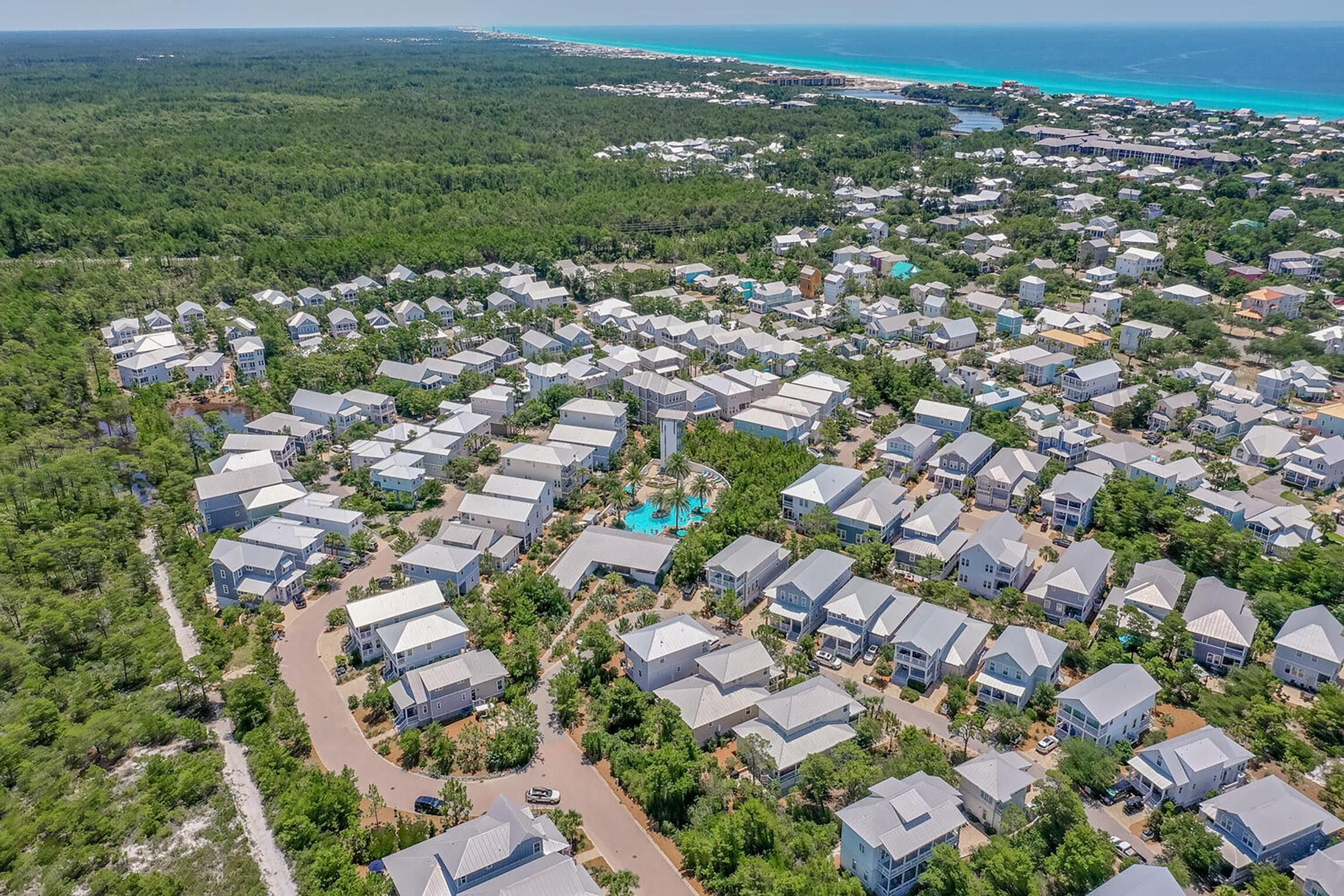 Vue aérienne d’un quartier résidentiel avec des maisons, des routes et une plage en arrière-plan.