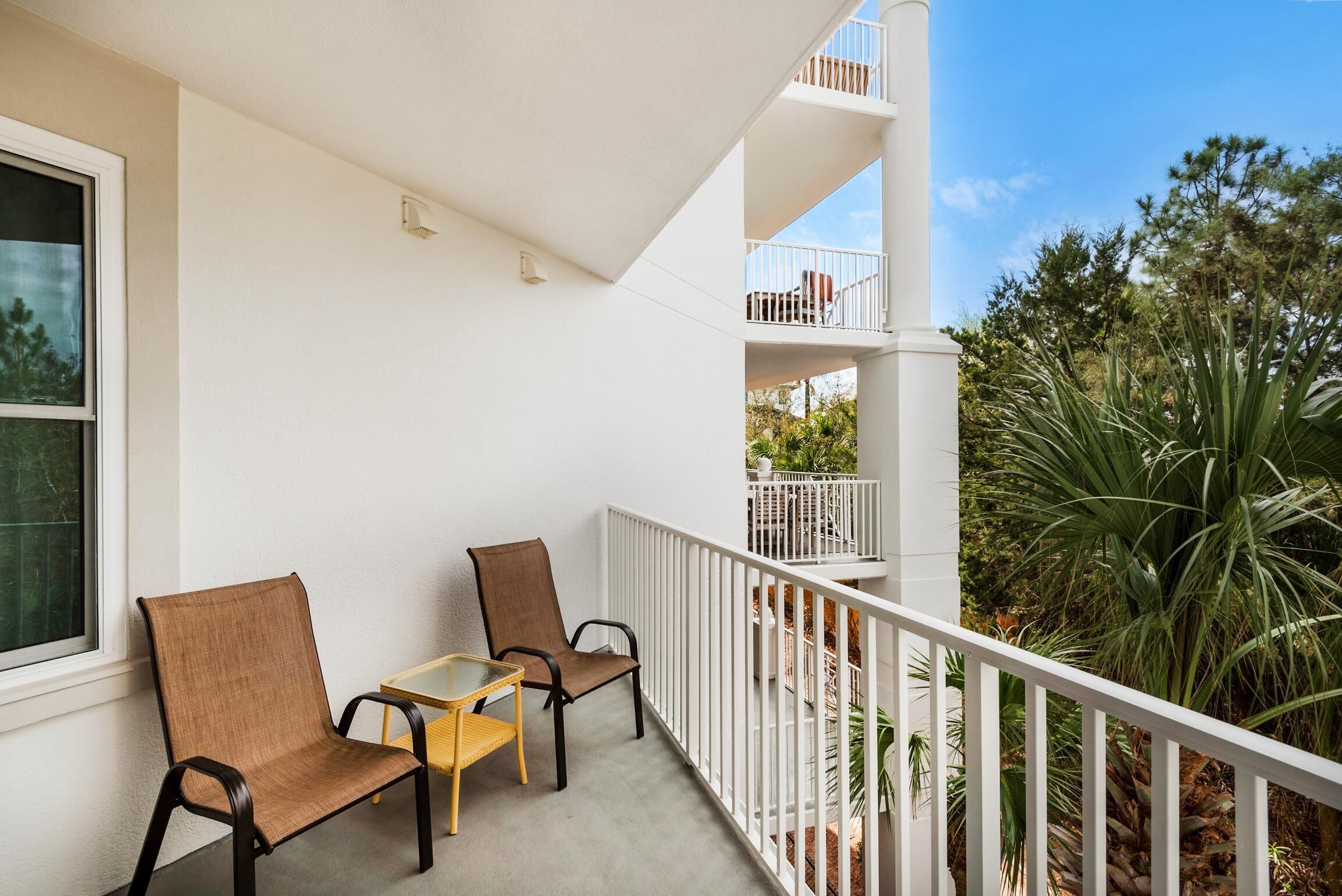 Un balcon avec deux chaises et une petite table, des balustrades blanches et une vue sur la verdure.