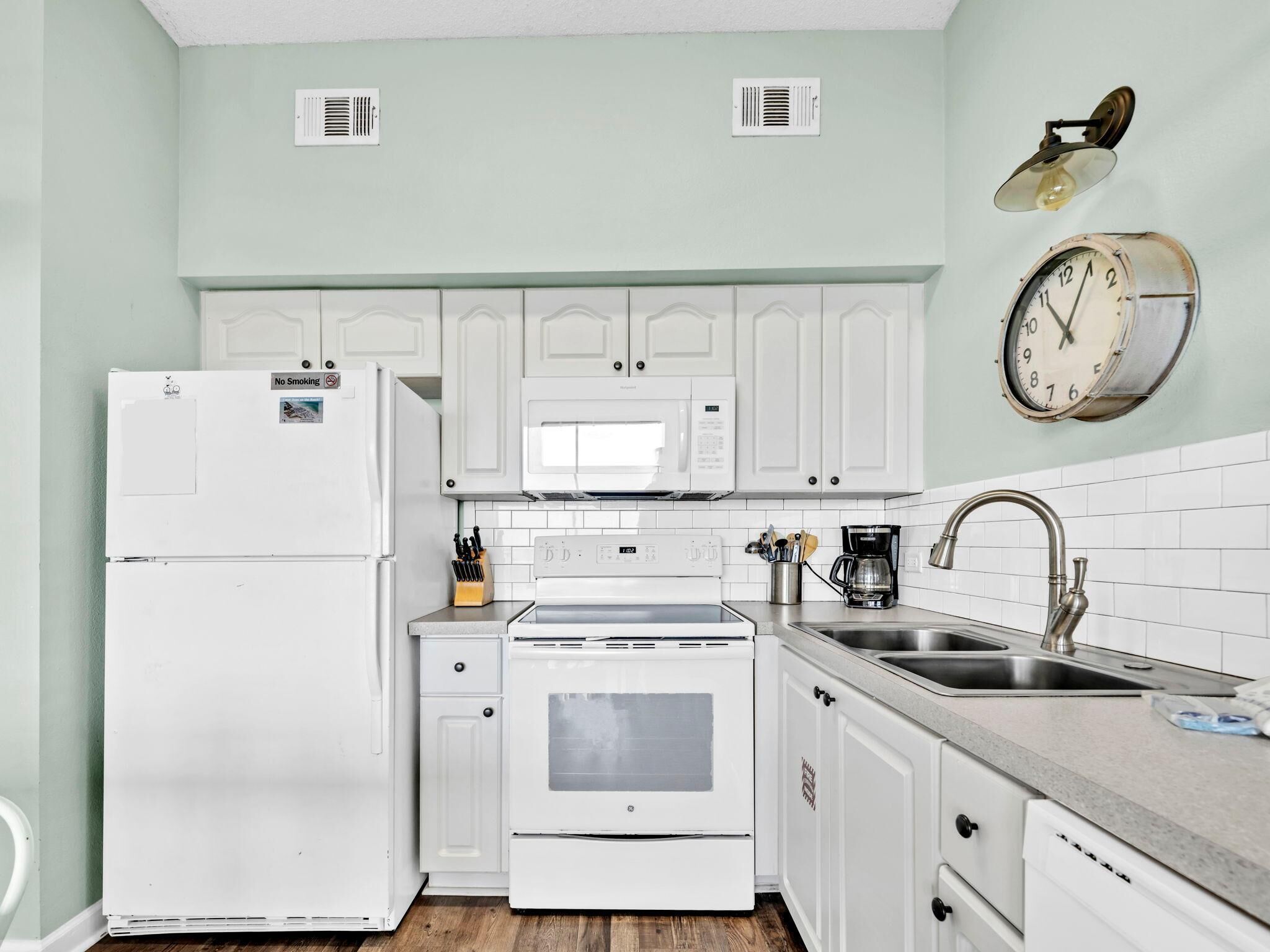 A kitchen with white cabinets, a microwave, a stove, a sink, and a clock on the wall.