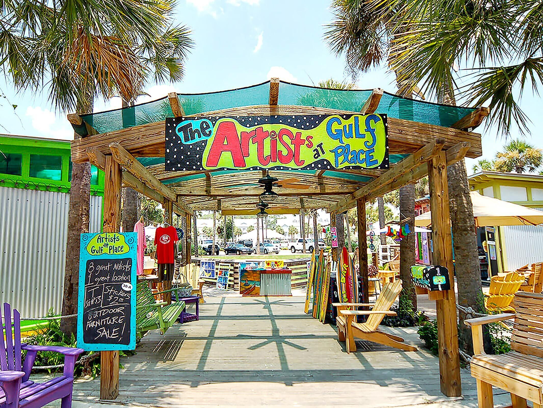 Un marché en plein air, avec une enseigne colorée sur laquelle on peut lire « Les artistes de Gulf Place », et un panneau noir annonçant une vente de meubles.