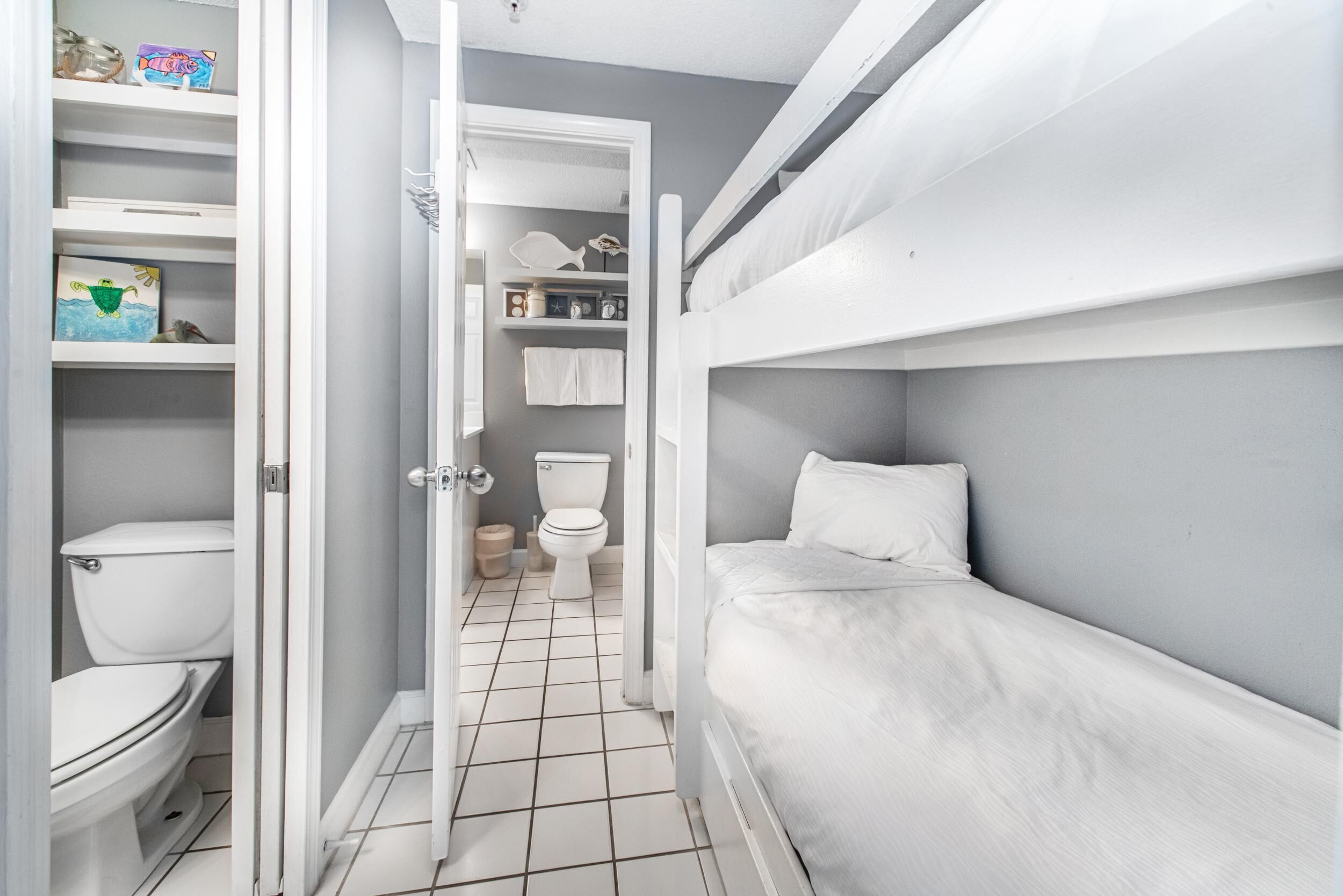Une petite pièce, de taille modeste, comprenant un lit superposé, des toilettes et une étagère contenant divers objets.