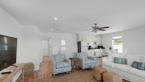 A modern living room with a TV, sofa, chairs, and a kitchen in the background.