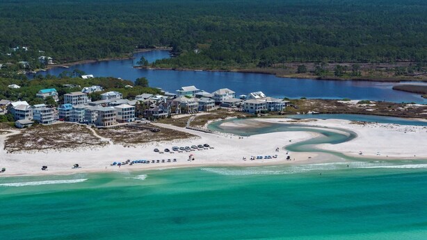 An aerial view of a coastal resort with multiple buildings, a sandy beach, and a large body of water.
