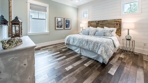 Quarto com cabeceira de madeira, cama com roupa de cama estampada, ventilador de teto e mesa de cabeceira com abajur.