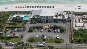 Vista aérea de um resort com piscina, guarda-sóis de praia e estacionamento.