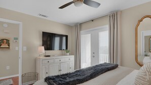 Ein Schlafzimmer mit Bett, Deckenventilator, Fernseher, Schminktisch und einem Fenster mit Vorhängen.