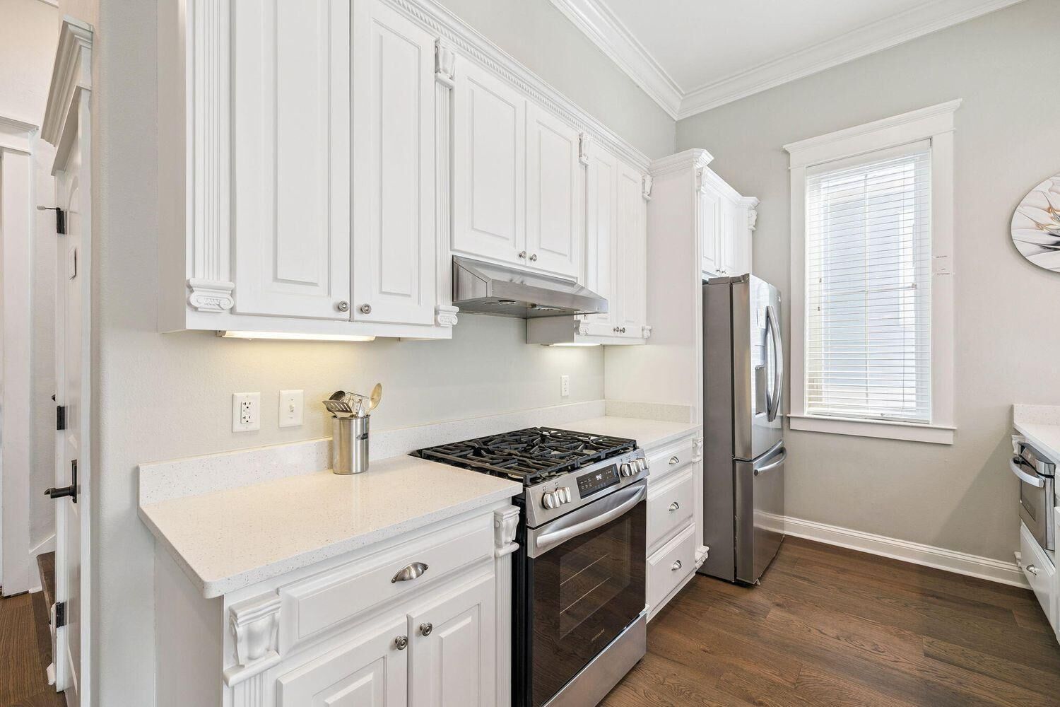 A kitchen with white cabinetry, a stainless steel stove, a refrigerator, and a window with blinds.