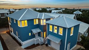 Uma casa de dois andares com fachada azul e telhado de metal, apresentando uma varanda frontal e uma garagem.