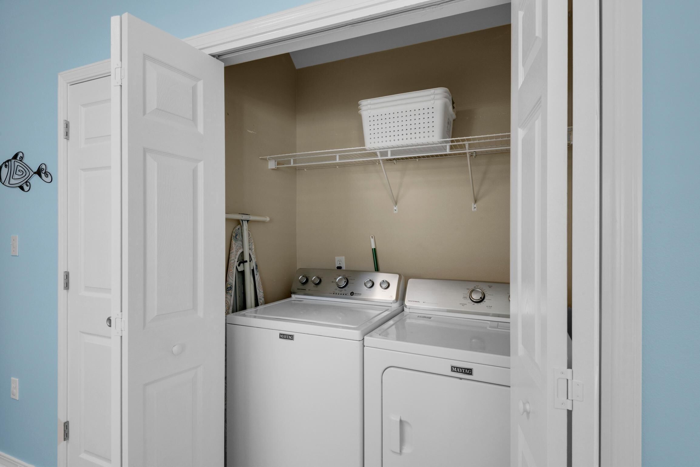 A laundry room with a white washer and dryer, a shelf above the dryer, and a door with a white handle.