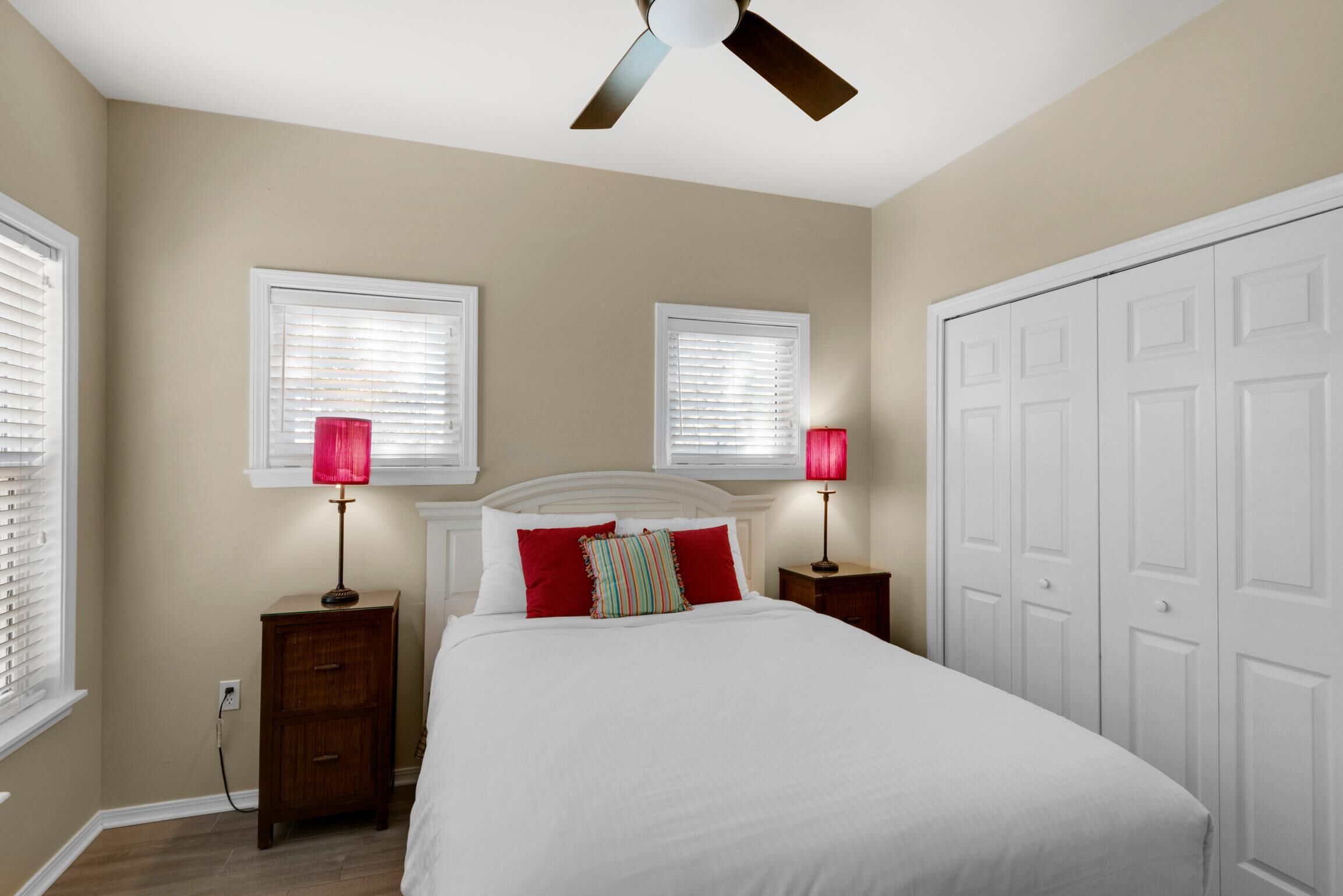 A bedroom with a bed, two bedside tables, a ceiling fan, and a wardrobe.