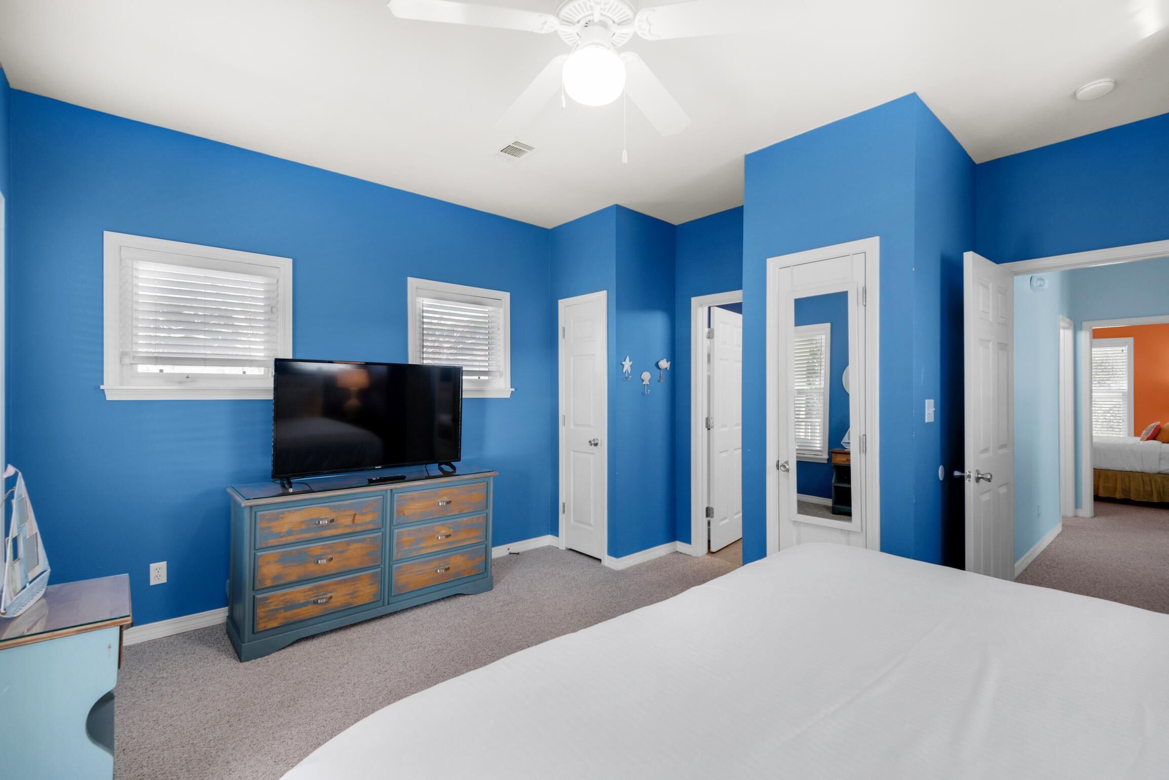 Camera da letto con pareti blu, un ventilatore a soffitto bianco, un letto, una cassettiera e una televisione.